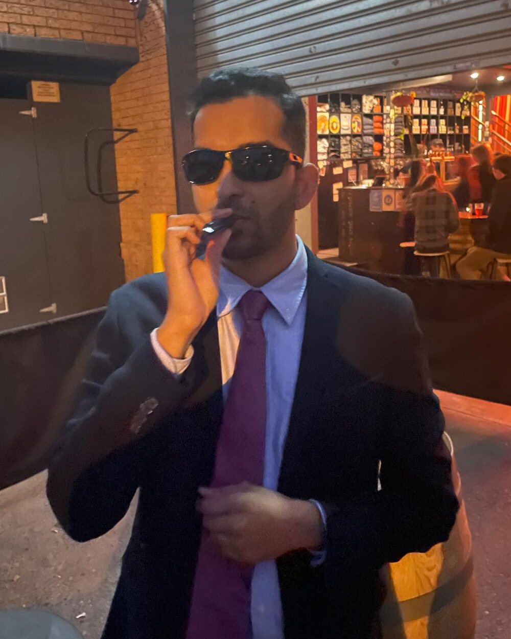 Mayuresh in sunglasses and a suit throwing up peace signs at a bar
