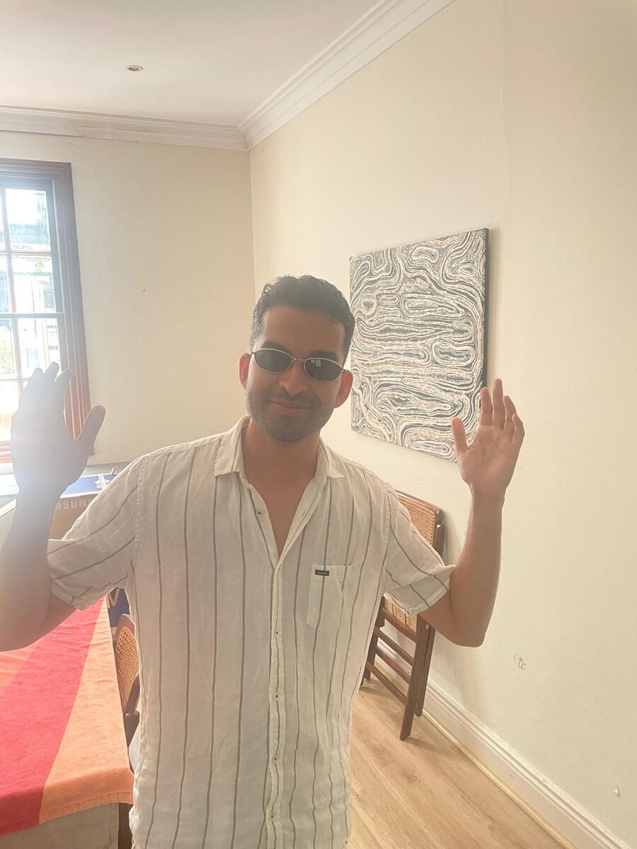 Mayuresh in a striped linen shirt and small sunglasses with both hands up