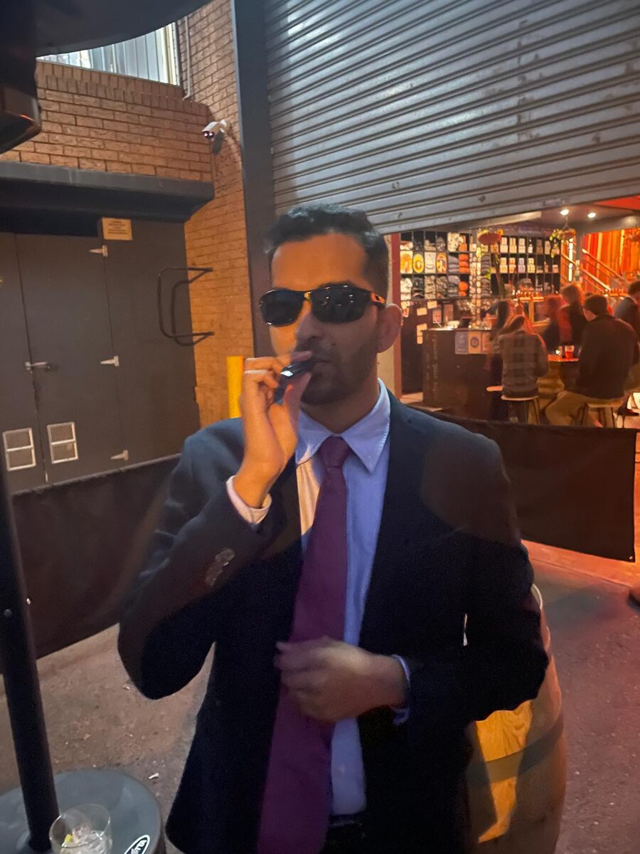 Mayuresh in a suit and sunglasses outside a bar at night